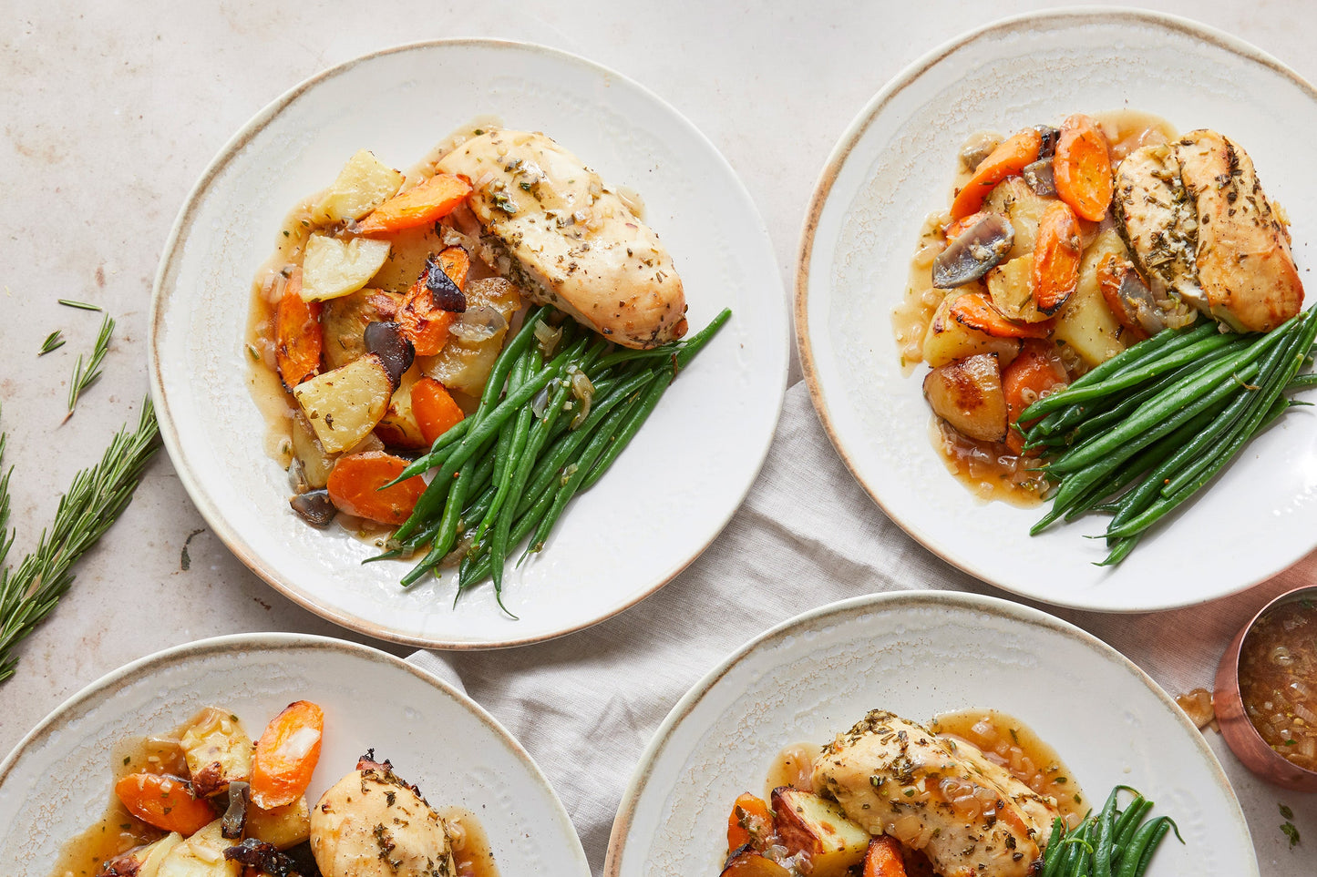 Plated chicken dinner with roasted potatoes and carrots with gravy and green beans on the side.