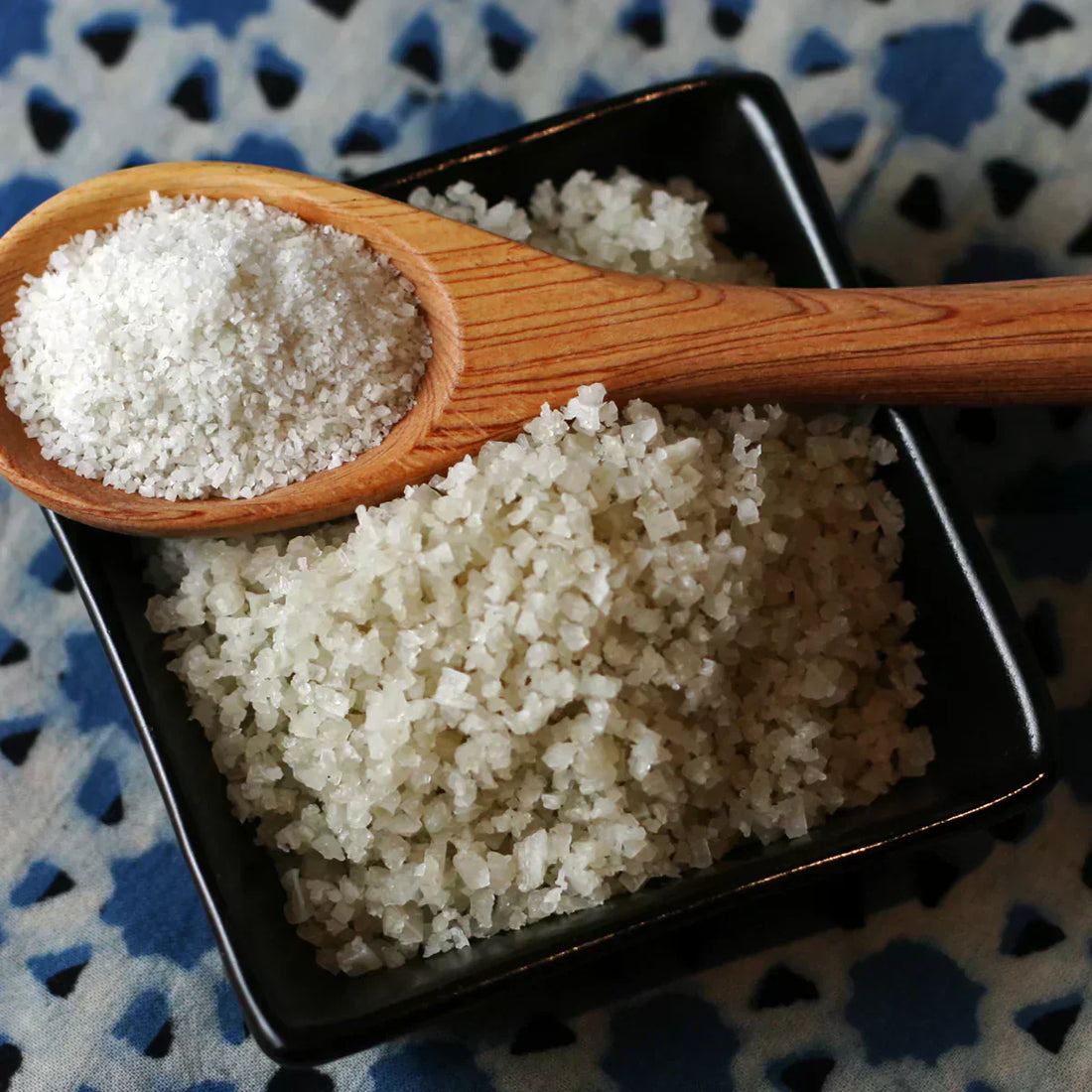 A square bowl or coarse sea salt with a wooden spoon of fine ground sea salt sitting across the top of the square bowl